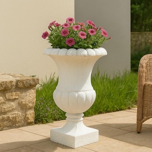 Peut inclure: Un pot de fleurs blanc orné, rempli de fleurs roses vibrantes. Le pot a une forme d'urne classique avec un bord cannelé et repose sur une base carrée. Les fleurs sont en pleine floraison, ajoutant une touche de couleur.