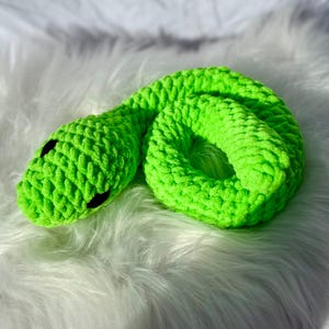 Peut inclure: Un jouet serpent en crochet de couleur vert vif. Le serpent est enroul&eacute; en cercle avec sa t&ecirc;te reposant sur son corps. Le serpent a des yeux noirs.