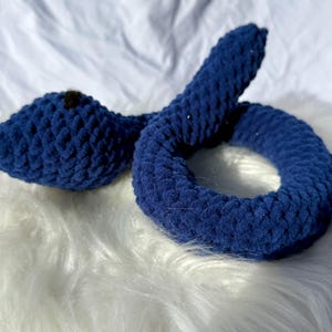 Peut inclure: Un jouet serpent en crochet bleu avec un nez noir. Le serpent est enroul&eacute; en cercle.