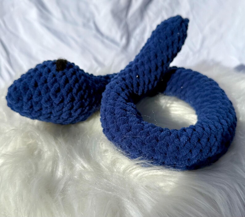 Peut inclure: Un jouet serpent en crochet bleu avec un nez noir. Le serpent est enroul&eacute; en cercle.