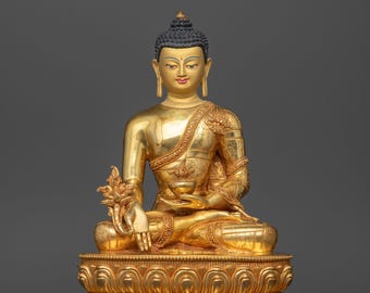 Pode incluir: Uma estátua de Buda de cor dourada em posição de lótus sentada sobre uma base de lótus dupla. A figura tem uma textura de cabelo azul escuro, traços faciais pintados e segura uma pequena tigela na mão esquerda sobre o joelho.