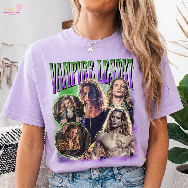 May include: A light purple short-sleeve t-shirt featuring a graphic print with the text VAMPIRE LESTAT in green and purple letters. The design includes four distinct photographic portraits of a long-haired person in various poses and settings.