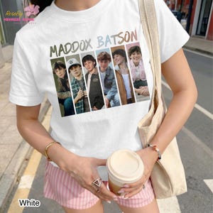 May include: A white short-sleeved t-shirt featuring a graphic print of the text MADDOX BATSON above five vertical panels, each displaying a different portrait of the same person wearing various outfits, including a jacket, shirt, and sweater.