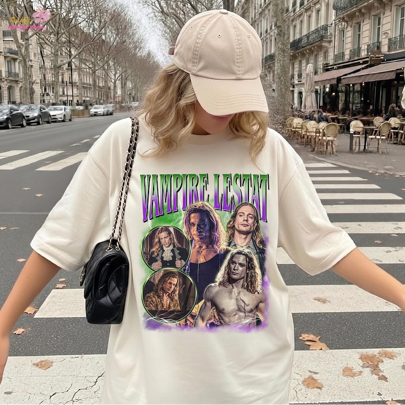 May include: A cream-coloured short-sleeve t-shirt featuring a graphic print with the text VAMPIRE LESTAT in green and purple letters. The design includes four distinct photographic portraits of a long-haired character in various poses.