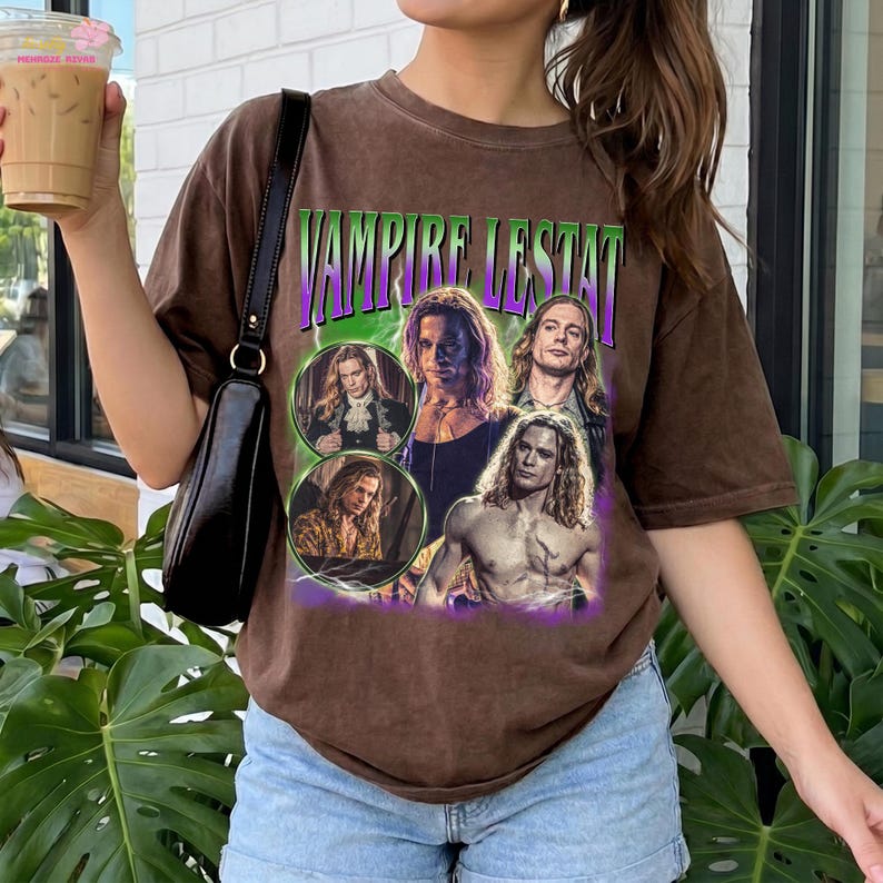 May include: A brown short-sleeved t-shirt featuring a graphic print with the text VAMPIRE LESTAT in green and purple letters. The design includes multiple photographic images of a long-haired character in various poses against a green lightning background.