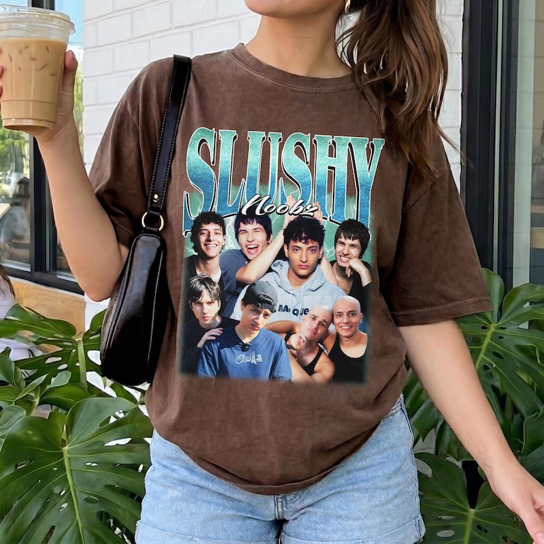 May include: A brown short-sleeve t-shirt featuring a graphic print with the text "SLUSHY Noobz" in a blue gradient font. The graphic displays a collage of six individuals in various poses, set against a light blue and green background.