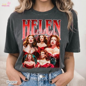May include: A charcoal grey short-sleeve t-shirt featuring the red text HELEN and Sharp in black script. The graphic displays four images of a red-haired person in a red dress, with a lightning-like background effect behind the central figures.
