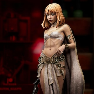 May include: A detailed figurine of a woman in a fantasy outfit, featuring a cream-colored top and skirt with gold accents. She has short, light orange hair and holds a curved blade. The figurine is labeled "KUZON".