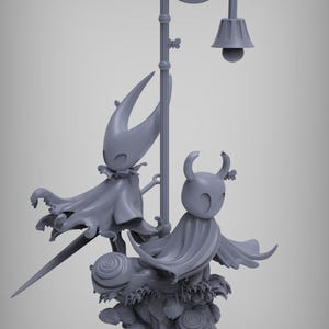 Puede incluir: Escultura gris con dos figuras estilizadas con capas, cerca de una farola decorativa. Las figuras están sobre una base con elementos florales y vegetales. La lámpara tiene un diseño en espiral.