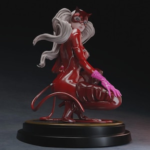 May include: A red figurine of a character in a cat-themed costume, with a mask and long white hair. The figure is posed in a crouching position, wearing pink gloves. The base is black with a gold trim.