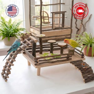 May include: A wooden bird play stand with multiple levels, ladders, and perches. The stand features a natural wood design and is adorned with small birds. A bird cage is visible in the background. The image includes a "Made in USA" logo.