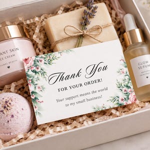 May include: A gift box containing a jar of Radiant Skin face cream, a bar of soap tied with twine and lavender, a bottle of Glow Serum with a dropper, a round bath bomb, and a Thank You for your order card decorated with floral illustrations.
