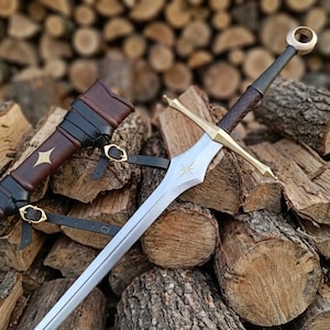 Pode incluir: Uma espada de aço com guarda de latão e punho revestido em couro castanho escuro com um pomo em forma de anel. A lâmina apresenta uma gravação de estrela dourada perto do punho. Acompanha uma bainha de couro castanho com tiras pretas.