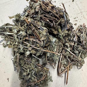 Puede incluir: Un montón de hierbas secas, con una mezcla de hojas y tallos marrones, verdes y beiges. Las hierbas parecen estar sueltas, con algunas piezas individuales dispersas. La imagen está tomada desde arriba, destacando la textura y los colores naturales.