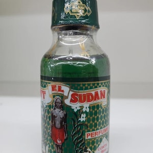 Puede incluir: Botella de perfume de vidrio transparente con líquido verde. La etiqueta dice "EL SUDAN PERFUME" y muestra una persona con falda roja. La botella tiene una tapa verde con el texto "WELBUSH HSBREM".
