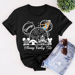 Puede incluir: Camiseta negra con un dise&ntilde;o gr&aacute;fico blanco con tem&aacute;tica de Disney. El dise&ntilde;o incluye el nombre "Ashley", un castillo, fuegos artificiales y el texto "Disney Family Trip".