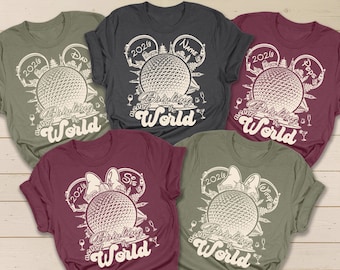 May include: Five t-shirts in various colors, each featuring a graphic design with the text "Drinking Around the World" and the year "2020" or "2026". The design includes a globe and Mickey Mouse ears.