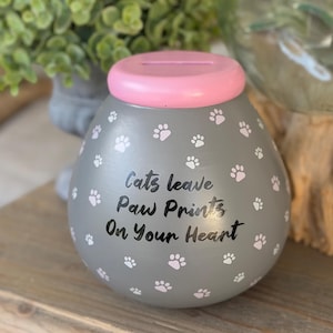 May include: A white ceramic mug with a black handle and the text "But First, Coffee" in a black, bold font. The mug is on a white surface.
