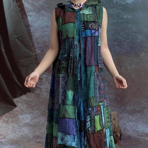 Può includere: Abito lungo senza maniche in patchwork verde, blu e marrone. L'abito presenta un cappuccio e una chiusura con fiocco sul davanti. Il tessuto sembra essere un materiale morbido e strutturato. L'abito è in stile bohémien.