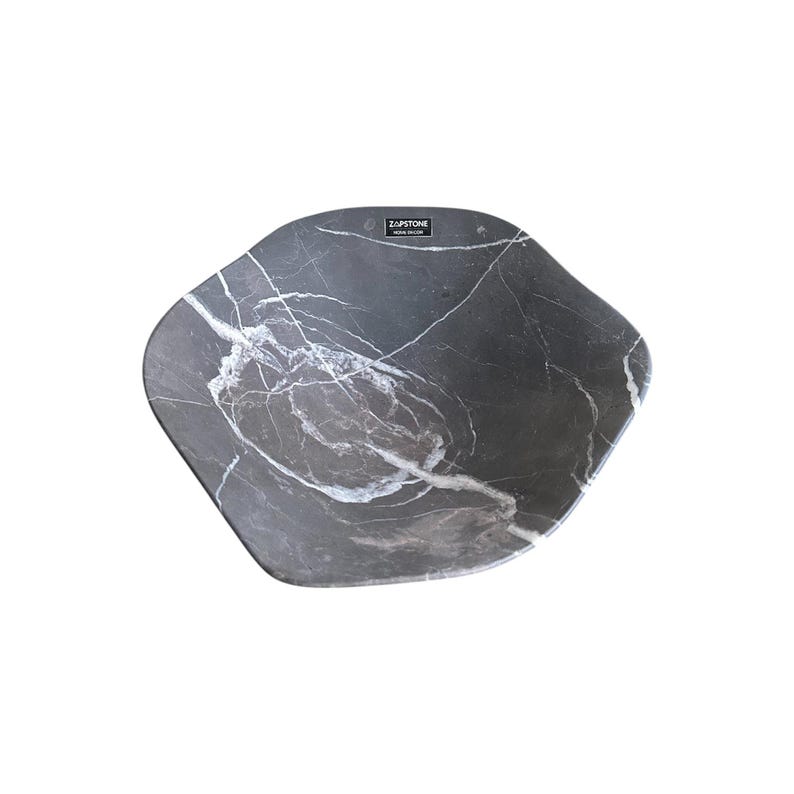 May include: A dark gray, marble-patterned decorative bowl with a unique, irregular shape. White veining runs throughout the bowl's surface. The brand name "ZAPSTONE" is printed on a small, rectangular label on the bowl.