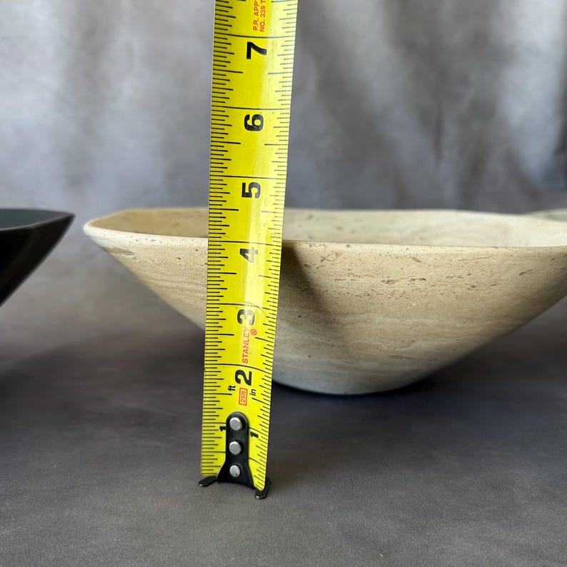 May include: A beige, square-shaped bowl with a textured surface. A yellow tape measure shows the bowl is approximately 6 inches in diameter. The bowl is set against a gray background.