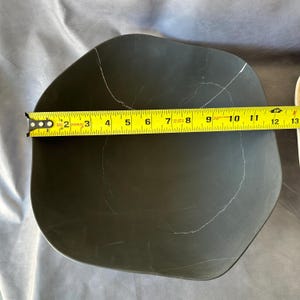 May include: A dark gray, irregularly shaped plate with white veining. The plate is approximately 12 inches in length, as measured by a yellow tape measure. The plate has a smooth surface and a modern design.