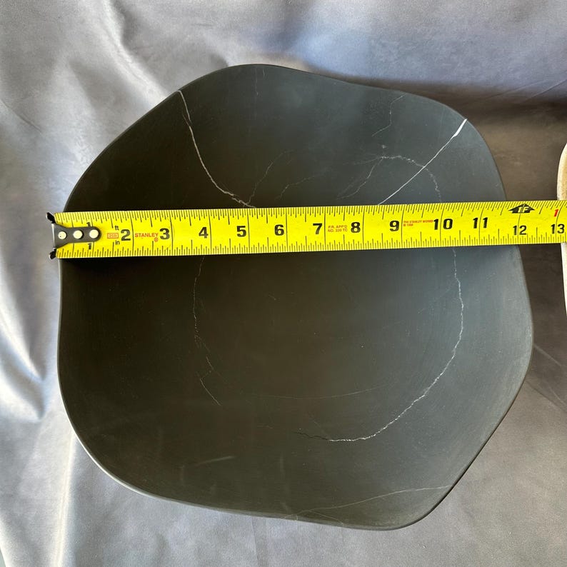 May include: A dark gray, irregularly shaped plate with white veining. The plate is approximately 12 inches in length, as measured by a yellow tape measure. The plate has a smooth surface and a modern design.