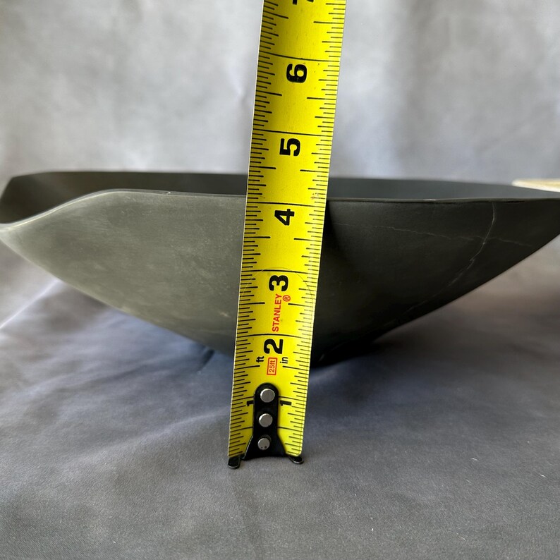 May include: A dark gray, square-shaped bowl with a wavy rim. The bowl is approximately 2 inches (5 cm) deep, as measured by a yellow measuring tape. The bowl's interior is not visible.