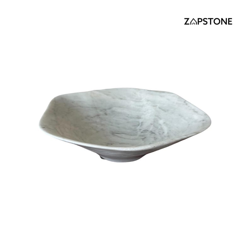 May include: A white and gray marble-patterned bowl with an irregular, organic shape. The bowl has a shallow depth and a slightly raised base. The brand name "ZAPSTONE" is printed in black on the upper right.