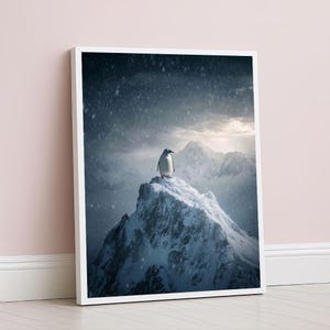 May include: A framed print featuring a penguin standing atop a snow-covered mountain peak. The artwork depicts a winter landscape with falling snow and a cloudy sky. The penguin is the focal point, set against a backdrop of snow-capped mountains.