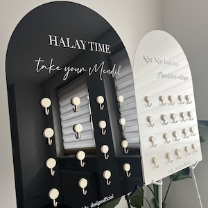 Puede incluir: Una pantalla arqueada en blanco y negro con ganchos para colgar objetos. La pantalla negra tiene el texto "HALAY TIME take your Mendil". La pantalla blanca tiene el texto "Ağır Ağır başlayın Mendilleri sallayın". Ambas pantallas tienen múltiples ganchos.