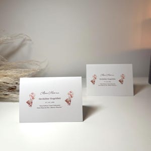 May include: Two white rectangular folded cards featuring a watercolor illustration of a brown teddy bear holding a cluster of pink balloons. The text reads Alara Mira'nın Mevlüdüne Hoşgeldiniz, 07 | 02 | 2026, and a Turkish phrase in black ink.