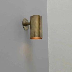 Könnte beinhalten: Zylindrische Wandleuchte aus Messing mit kreisförmiger Montageplatte. Die Leuchte hat einen warmen, goldenen Farbton und strahlt ein weiches, einladendes Licht aus. Das Design ist minimalistisch und modern, passend für verschiedene Einrichtungsstile.