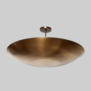 Könnte beinhalten: Eine große, bronzefarbene Pendelleuchte mit einem flachen, schalenförmigen Schirm. Die Leuchte wird von einer kleinen, kreisförmigen Deckenhalterung abgehängt. Der Schirm hat eine glatte, metallische Oberfläche und ein leicht gebogenes Profil.