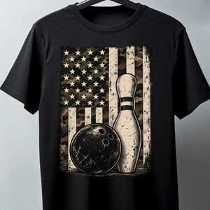 May include: A black short-sleeve t-shirt featuring a central graphic print. The design displays a bowling ball and a single bowling pin positioned in front of a distressed American flag pattern rendered in shades of green, brown, and tan camouflage.