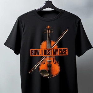 以下が含まれることがあります： 黒の半袖Tシャツで、茶色の木製バイオリンと斜めに置かれた弓のグラフィックが描かれています。バイオリンの中央にはオレンジ色の長方形のバナーがあり、黒い文字で「BOW, I REST MY CASE」と書かれています。