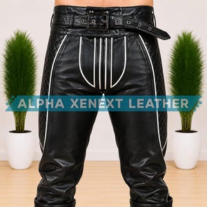 May include: Black leather pants featuring a high-waisted belt with a metal buckle, quilted side panels, and white piping accents. The front displays vertical white stripes and the text ALPHA XENEXT LEATHER across the center of the garment.