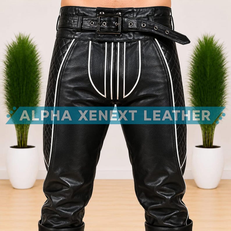 May include: Black leather pants featuring a high-waisted belt with a metal buckle, quilted side panels, and white piping accents. The front displays vertical white stripes and the text ALPHA XENEXT LEATHER across the center of the garment.