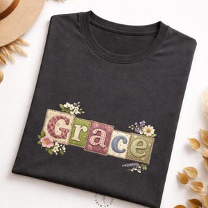 May include: A dark grey t-shirt with the word "Grace" in a patchwork design. Each letter is on a different square with floral accents. The squares have various patterns and colours, including pink, green, blue, and purple.