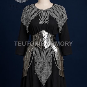 May include: A medieval outfit displayed on a mannequin. The outfit features a black dress, a silver metal corset, and a chainmail collar and skirt. The text "TEUTONIC ARMORY" is visible. A helmet logo is in the upper left corner.