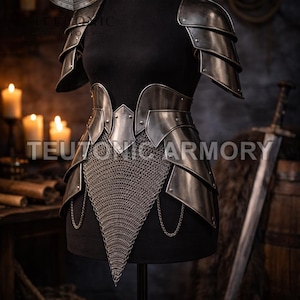 May include: A suit of medieval-style metal armour on a black mannequin. The armour includes layered shoulder pauldrons, a waist belt, and a chainmail skirt. The text "TEUTONIC ARMORY" is visible.