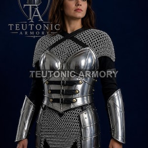 May include: A polished steel breastplate with black leather straps and buckles, worn over a chainmail hauberk. The armour set includes matching steel forearm bracers and a chainmail skirt. The text TEUTONIC ARMORY is visible on the chest and logo.