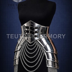 May include: A silver metal armour piece, displayed on a black mannequin. The armour features a waist belt with two black leather straps and hanging chainmail. The text "TEUTONIC ARMORY" is visible.