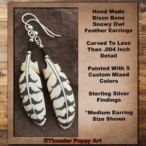 May include: Handmade bison bone feather earrings, featuring a snowy owl design. The earrings are carved with intricate detail and painted with five custom colors. Sterling silver findings complete the design. The text on the image says "Medium Earring Size Shown."