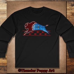 May include: Black long-sleeve shirt featuring a Native American-inspired design. The graphic includes a bison silhouette in burgundy and blue, with a crescent moon and star details. The text "Thunder Puppy Art" is at the bottom.