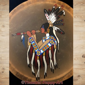 May include: A hand-painted Native American drum featuring a depiction of a person playing a flute. The person is wearing a headdress with feathers and traditional clothing. The drum is brown with a painted design in red, blue, yellow, and white.