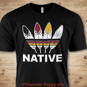 Może przedstawiać: Czarny T-shirt z białym nadrukiem czterech stylizowanych piór w kolorze czerwonym, żółtym, białym i czarnym. Pióra są ułożone w kształcie korony z poziomym wzorem pasków poniżej. Słowo "NATIVE" jest nadrukowane na biało pod piórami.