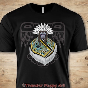 Puede incluir: Camiseta negra con un gráfico colorido de una figura nativa americana con un tocado y ropa tradicional. El gráfico está rodeado por un diseño de águila estilizado. El texto "Thunder Puppy Art" está en la parte inferior de la camiseta.
