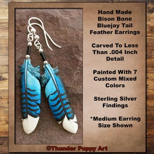 May include: Handmade bison bone earrings featuring bluejay tail feathers. The earrings are painted with seven custom mixed colors and have sterling silver findings. The medium-sized earrings are carved with fine detail.