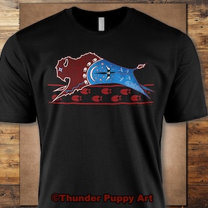 May include: Black t-shirt featuring a stylized bison design. The bison is depicted in shades of red and blue with a crescent moon and star motif. The design includes a red border with floral elements. The text "Thunder Puppy Art" is at the bottom.